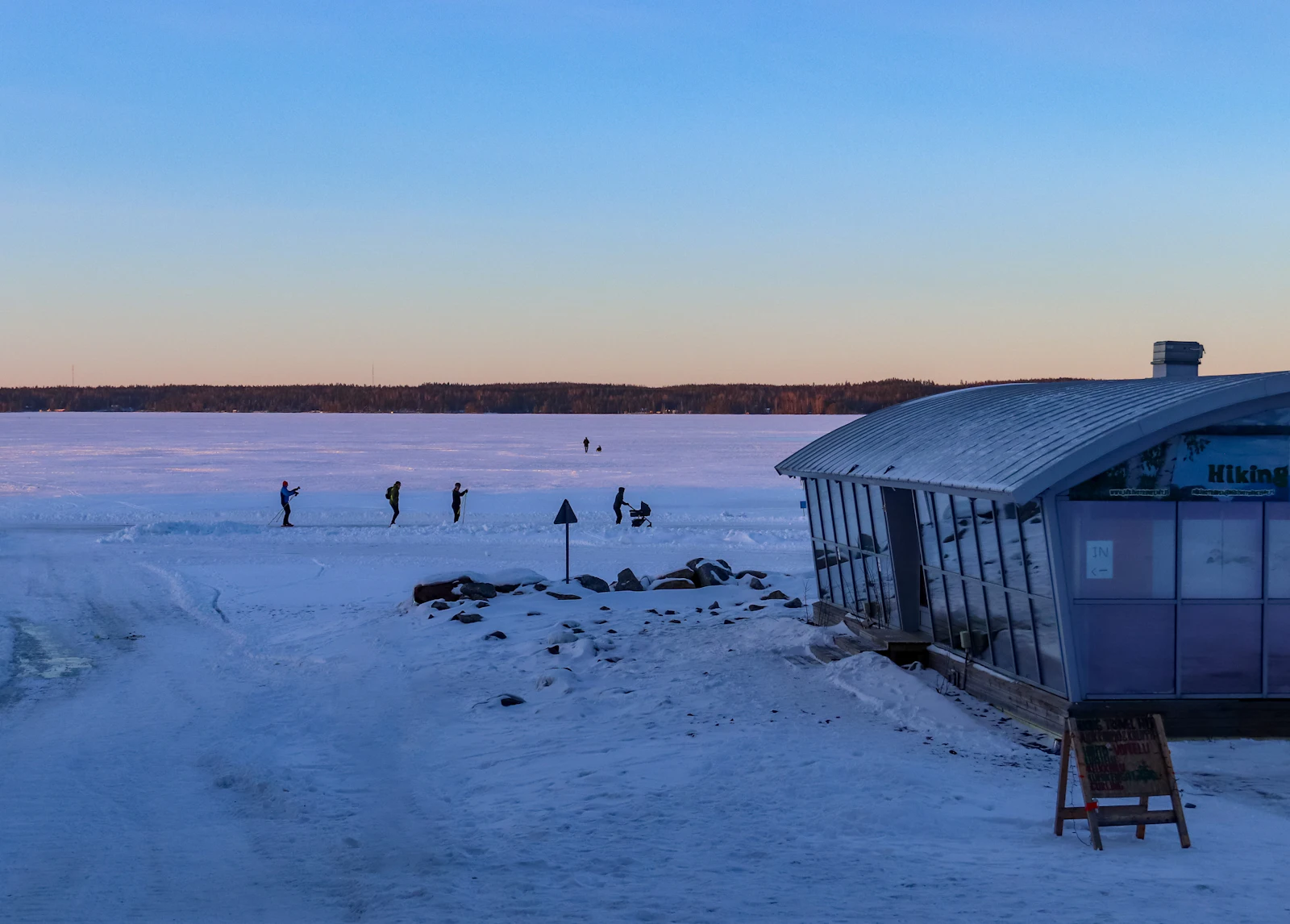 Talvinen järvi, rantasauna ja kävelijöitä jäällä